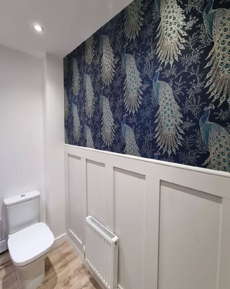 Powder room with navy peacock feature wallpaper above white board-and-batten wainscoting